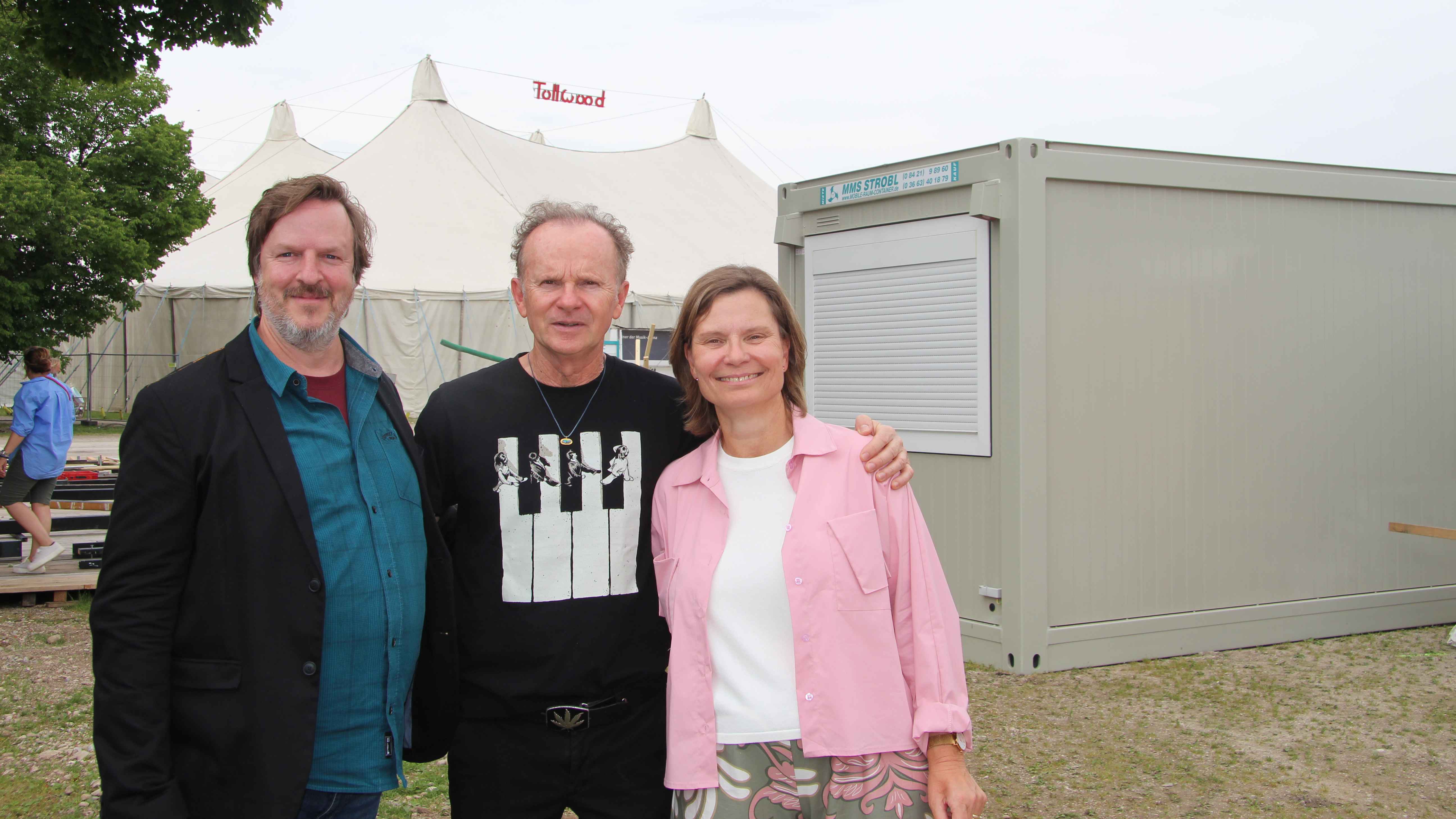 Stellten vor dem Musikzelt (im Hintergrund) das Tollwood-Programm 2025 vor: Mathias Schaettgen (links, Phi/Sch Art), Willy Astor und Stefanie Kneer (Tollwood).