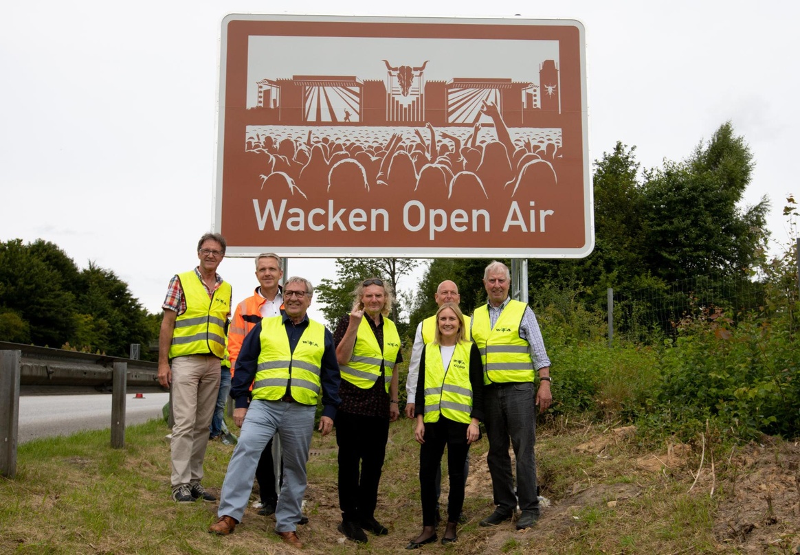 Vor dem Hinweisschild: die Enthüllungsdelegation mit Wacken-Veranstalter Holger Hübner (Mitte) und Amtsträgern aus Region und Land