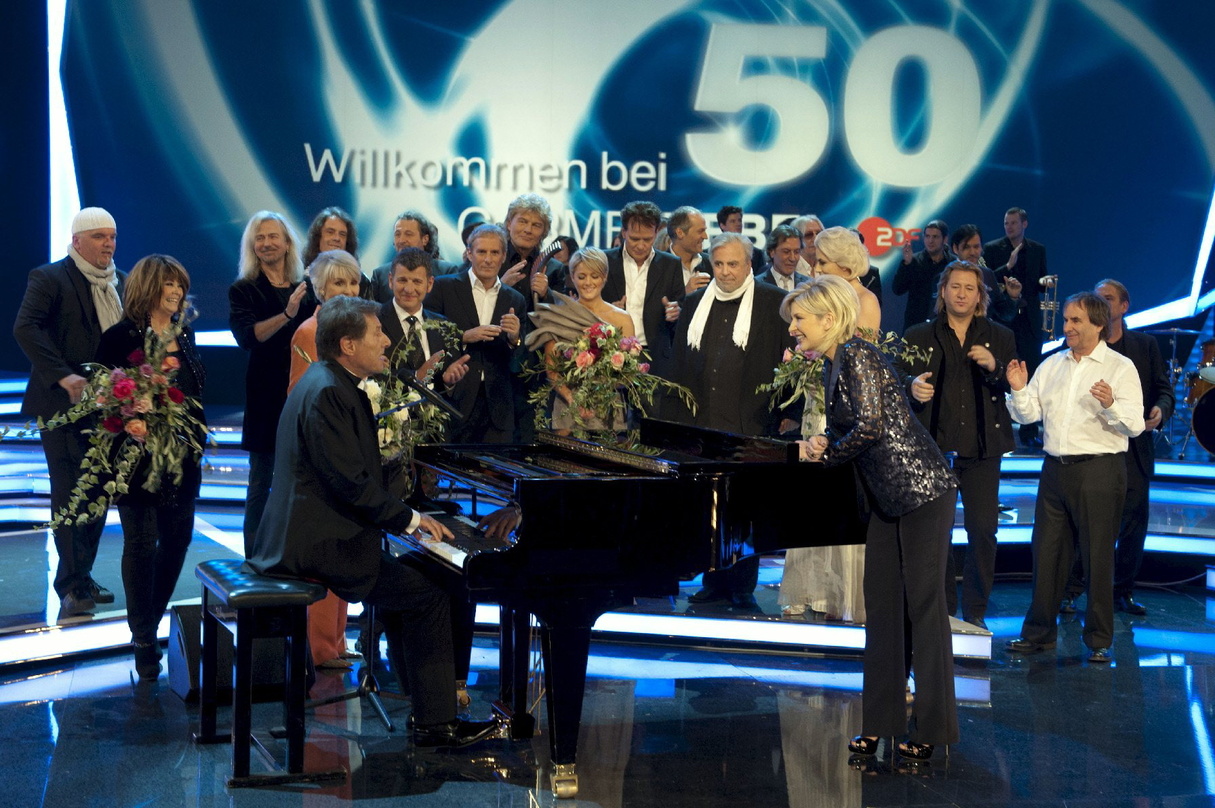 Fühlten sich alle "Willkommen": Carmen Nebel (vor dem Klavier, r.) mit Jubiläumsgästen von Udo Jürgens (am Klavier) über DJ Ötzi und Wencke Myhre bis zu Helene Fischer und Semino Rossi