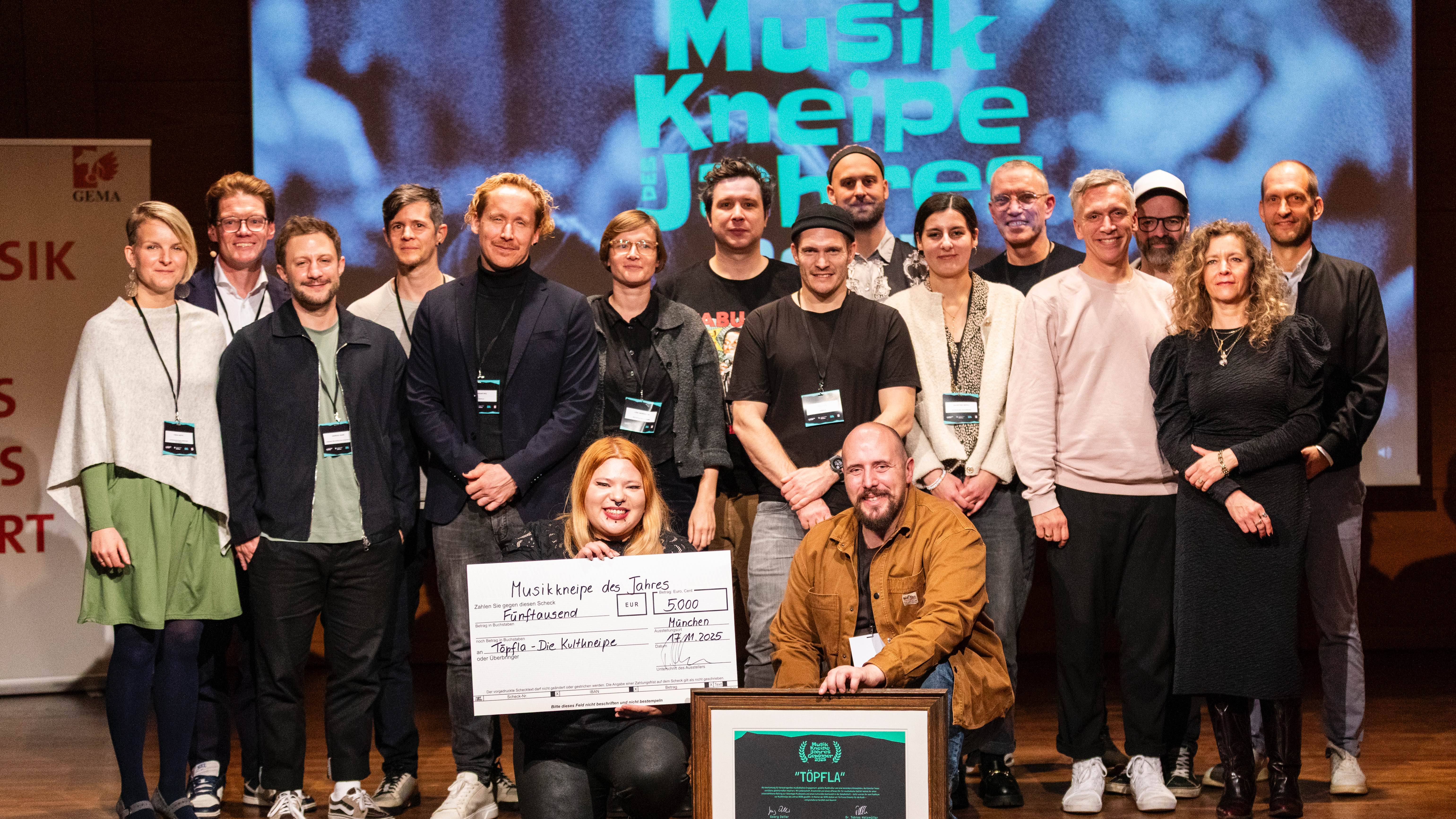 58bf22d1 d780 456c a115 2ff5680a3c65 Bei der Preisverleihung an die "Musikkneipe des Jahres 2025" am 17. November in den Räumlichkeiten des Gasteig: die Preisträgerinnen Nikki und Christoph Geiger (vorn, mit Preisgeldscheck u...