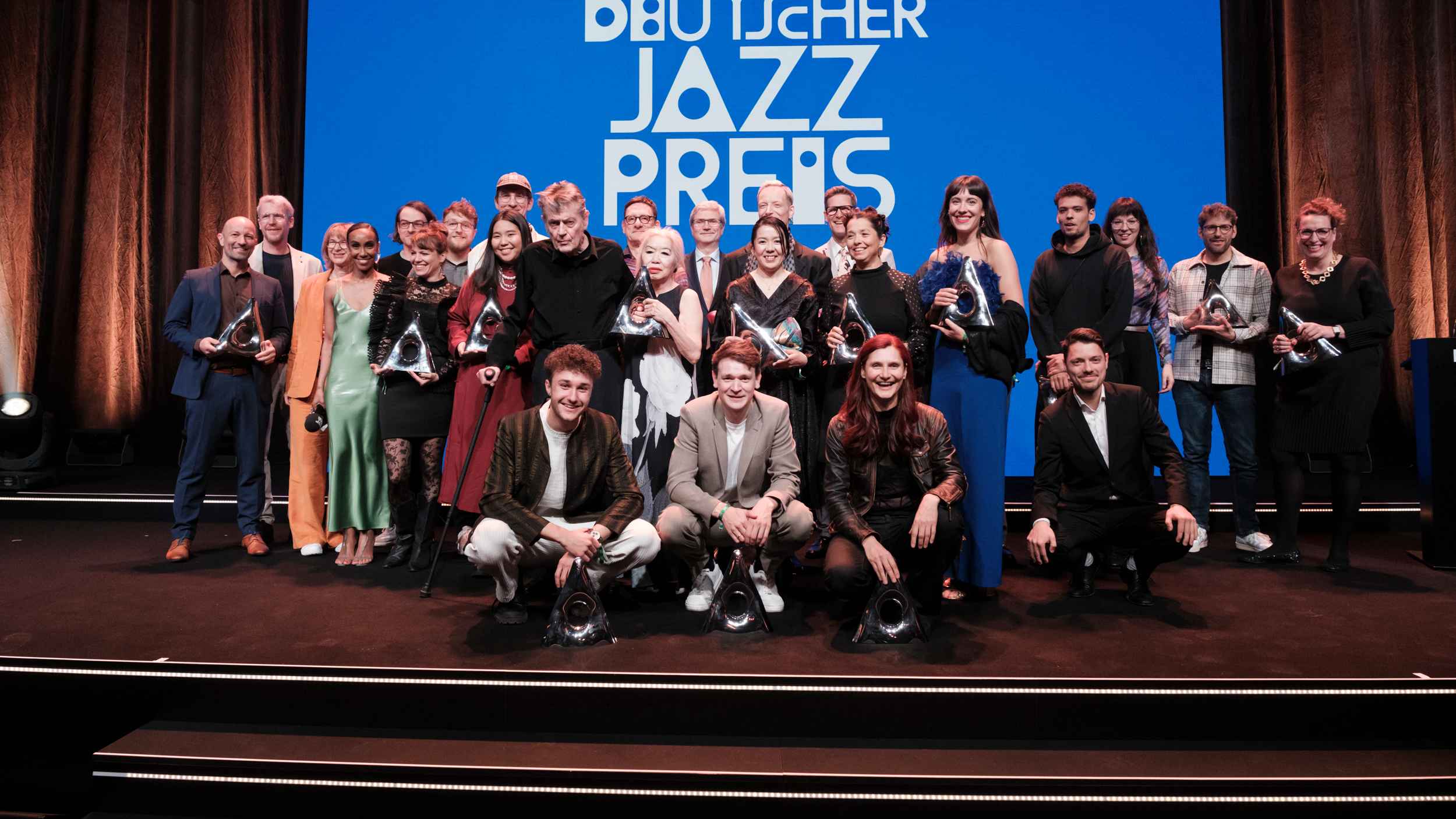 Posierten mit ihren Awards und den Moderator:innen: Die Preisträger:innen des Deutschen Jazzpreises.