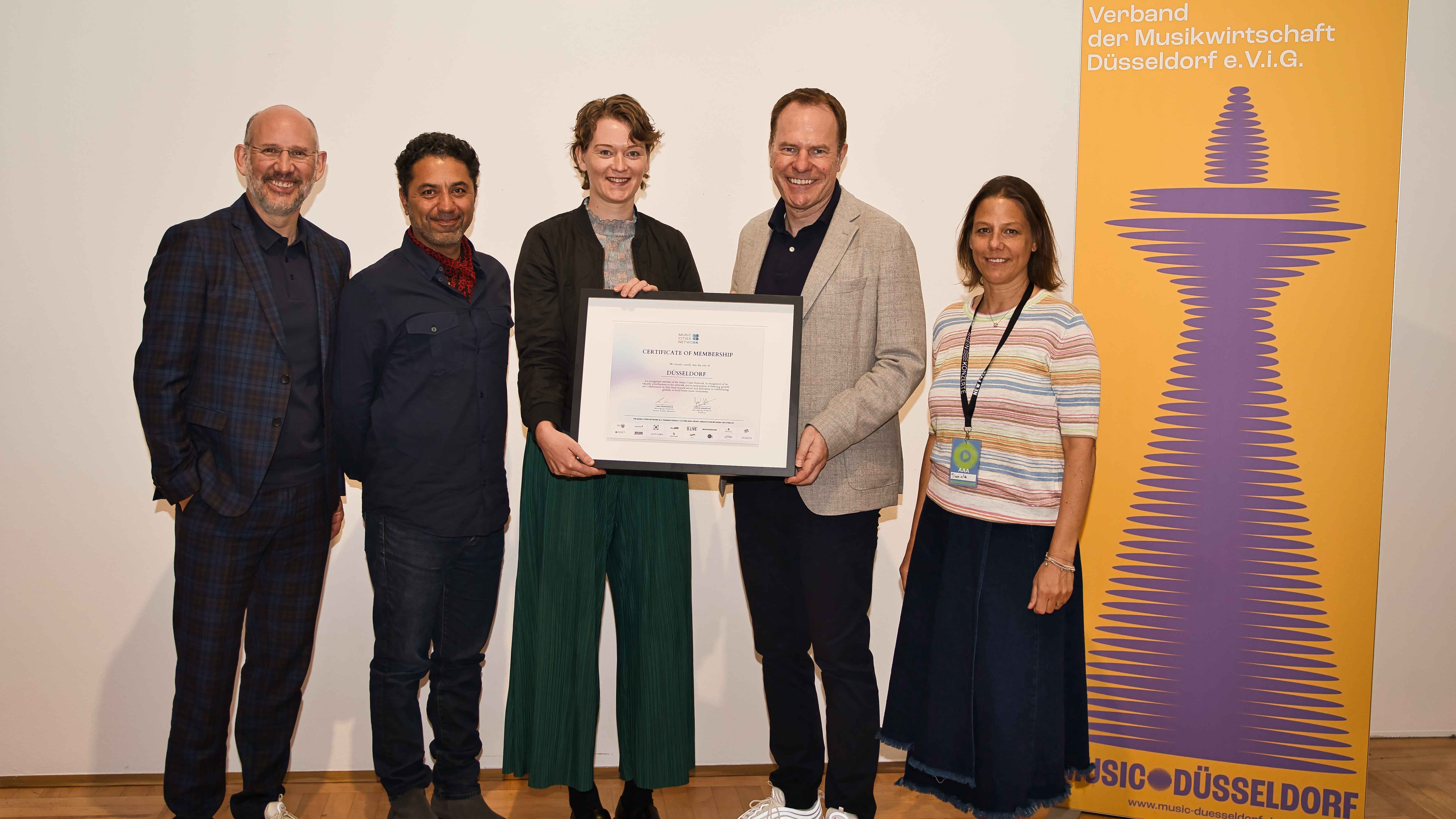 Präsentieren das Mitgliedszertifikat vom Music Cities Network (von links): Michael Brill (CEO D.Live), Hamed Shahi (CEO SSC Group), Lena Ingwersen (Geschäftsführerin Music Cities Network),...