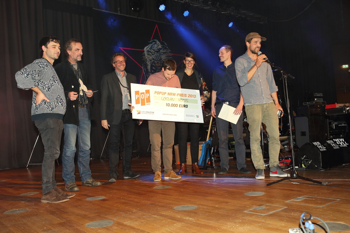 Ausgezeichnet: Die Siegerband Urban Homes mit Scheck und den popUP-NRW-Initiatoren auf der Bühne der Tonhalle